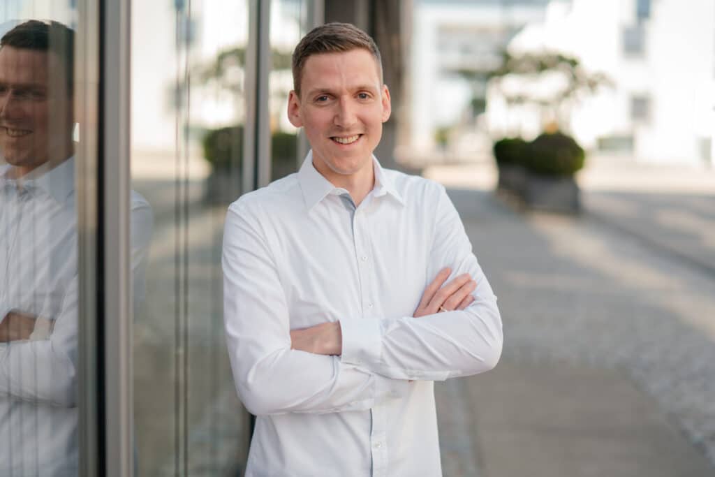 Bewerbungsfoto Ausbildung: 5 Tipps für Deine erste Bewerbung 2 Portraitbild eine jungen Mannes in einem weißen Hemd mit überkreuzten Armen. -Bewerbungsfoto Ausbildung